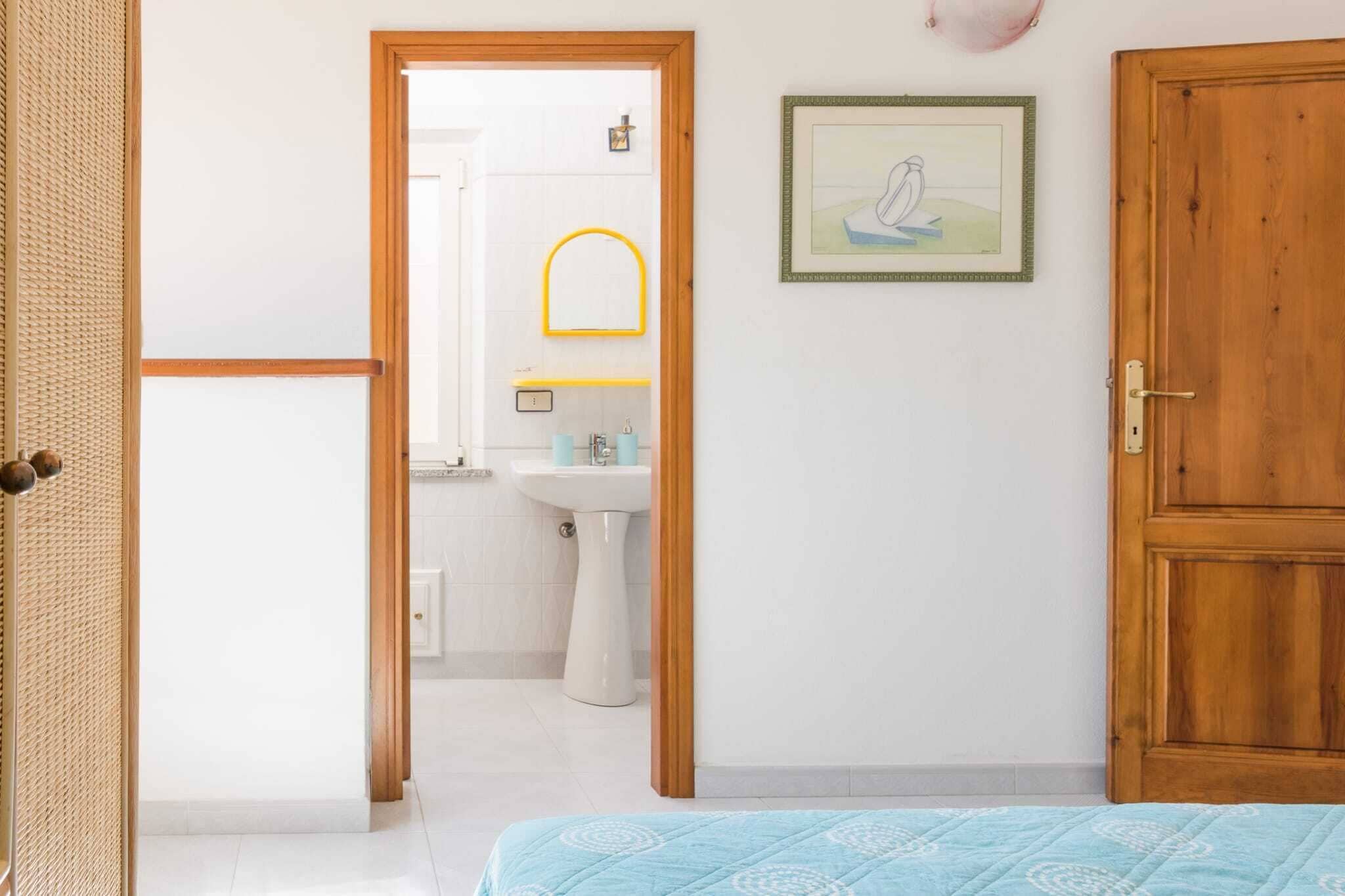 Une pièce avec un lit, une porte en bois, un tableau encadré et une salle de bain visible à travers une porte ouverte.
