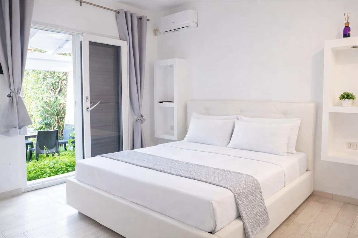 Un dormitorio moderno con una cama, un armario blanco, un estante pequeño y vistas a zonas verdes.