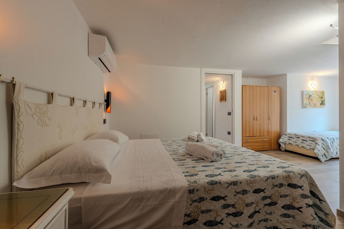 Una habitación de hotel con cama, mesita de noche, armario y una puerta que da a otra habitación.