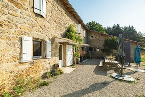 A stone building with a gravel courtyard, outdoor seating, and umbrellas. - Holiday Home 'Gîte Les Combes Claires' with Mountain View and Wi-Fi (Belsentes)