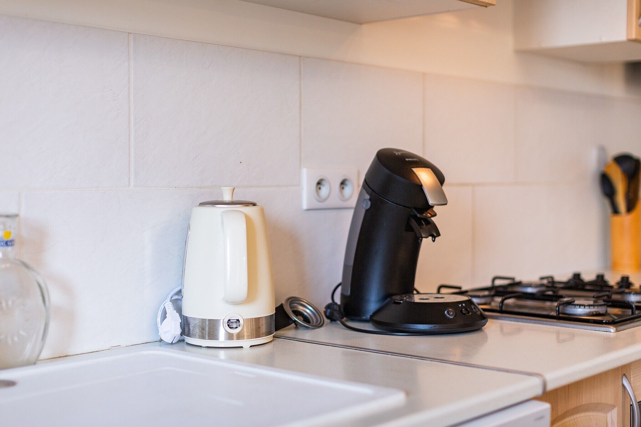 Uma cozinha com uma chaleira branca, uma cafeteira preta e um fogão.
