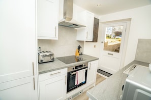 A modern kitchen with white cabinets, a built-in oven, a toaster, and a window with a view. - The Residence by Guestz (Cheltenham)