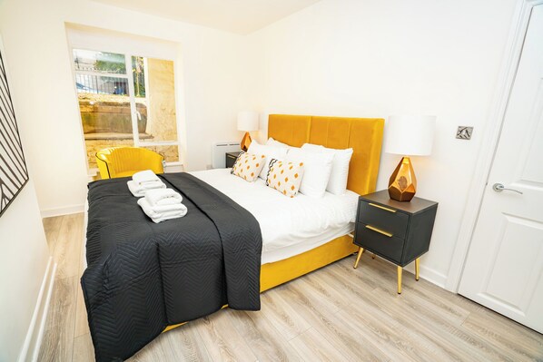 A hotel room with a bed, a bedside table, a chair, and a window. - The Residence by Guestz (Cheltenham)