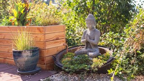 En trädgård med en trälåda som används som planteringslåda, en krukväxt och en Buddha-staty.
