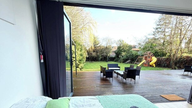 A bedroom with a large bed, green and white bedding, a green area rug, and a view of an outdoor deck with outdoor furniture.