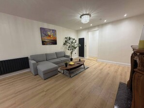 A modern living room with a grey sectional sofa, a wooden coffee table, a floor lamp, and a painting on the wall. - 2 Bed - Sleeps 4 - Hot Tub & Bbq (London)