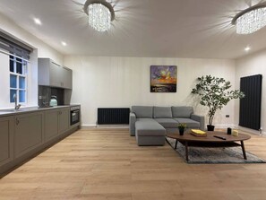 A modern kitchen with grey cabinets, a dining area with a grey sofa, a coffee table, and a painting on the wall.