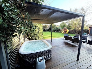 A hot tub under a covered patio with a view of a backyard.