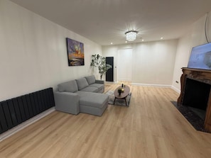 A modern living room with a sectional sofa, a small round table, a fireplace, and a painting on the wall. - 2 Bed - Sleeps 4 - Hot Tub & Bbq (London)