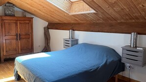 A bedroom with a sloped ceiling, wooden beams, a skylight, a bed, a wardrobe, and a heater. - Bed and Breakfast 'Framboise' with Shared Terrace, Shared Garden and Wi-Fi (Belsentes)