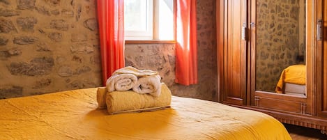 Une chambre avec un lit, une fenêtre avec des rideaux, un miroir et une armoire en bois.