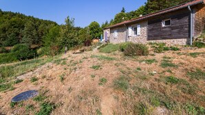 A stone house with a red-tiled roof, surrounded by dry grass and trees.