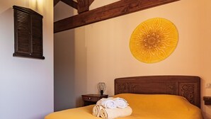 Ein Schlafzimmer mit hölzernem Kopfteil, einem Bett mit gelber Bettdecke, einer Wandlampe und einem dekorativen, runden Wandbild.