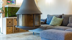 A modern living room with a large, metallic fireplace, a grey sofa, and a decorative painting on the wall.