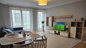 Una sala de estar moderna con sofá, mesa de comedor, sillas, televisor y una planta.