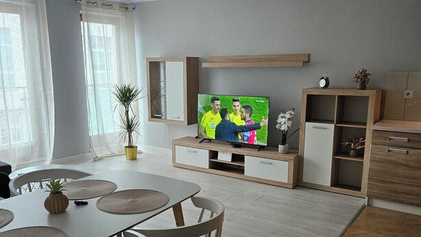 Una sala de estar moderna con televisor, mesa de comedor, sillas y una planta en maceta.
