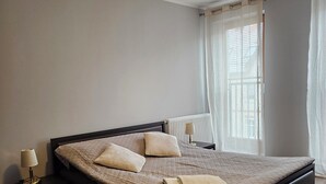 Un dormitorio con cama, mesita de noche, lámpara y ventana con cortinas.