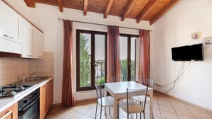 A kitchen with a stove, oven, and sink, a dining table with chairs, and a TV mounted on the wall. - Apartment 'Appartamento Borgo' with Mountain View, Wi-Fi and Air Conditioning (San Felice del Benaco)