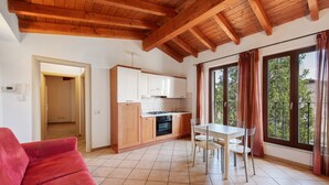 A compact kitchen with wooden cabinets, a dining table with chairs, and a red sofa. - Apartment 'Appartamento Borgo' with Mountain View, Wi-Fi and Air Conditioning (San Felice del Benaco)