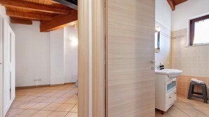 A room with a wooden ceiling, a white door, a bathroom with a sink and a stool, and tiled flooring. - Apartment 'Appartamento Borgo' with Mountain View, Wi-Fi and Air Conditioning (San Felice del Benaco)