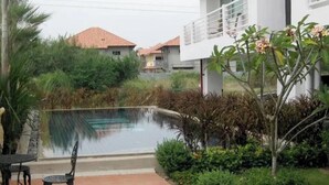 A swimming pool with a patio area, surrounded by greenery and a building with a balcony. - Large Condo Middle of Jomtien, Near the Beach 42m2 (Pattaya)