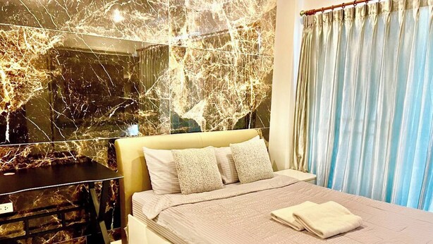 A modern bedroom with a marble wall, a bed with a beige headboard, and a bedside table. - Large Condo Middle of Jomtien, Near the Beach 42m2 (Pattaya)