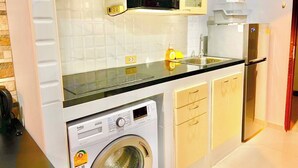 A compact kitchen with a washing machine, microwave, and a refrigerator. - Large Condo Middle of Jomtien, Near the Beach 42m2 (Pattaya)