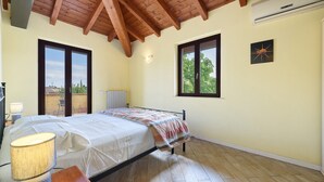 Une chambre à coucher avec un lit, un plancher en bois, de grandes fenêtres et un appareil de climatisation.