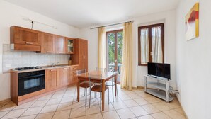 A kitchen with wooden cabinets, a stove, and a dining table with chairs. - Apartment 'San Felice' with Private Terrace, Wi-Fi and Air Conditioning (San Felice del Benaco)