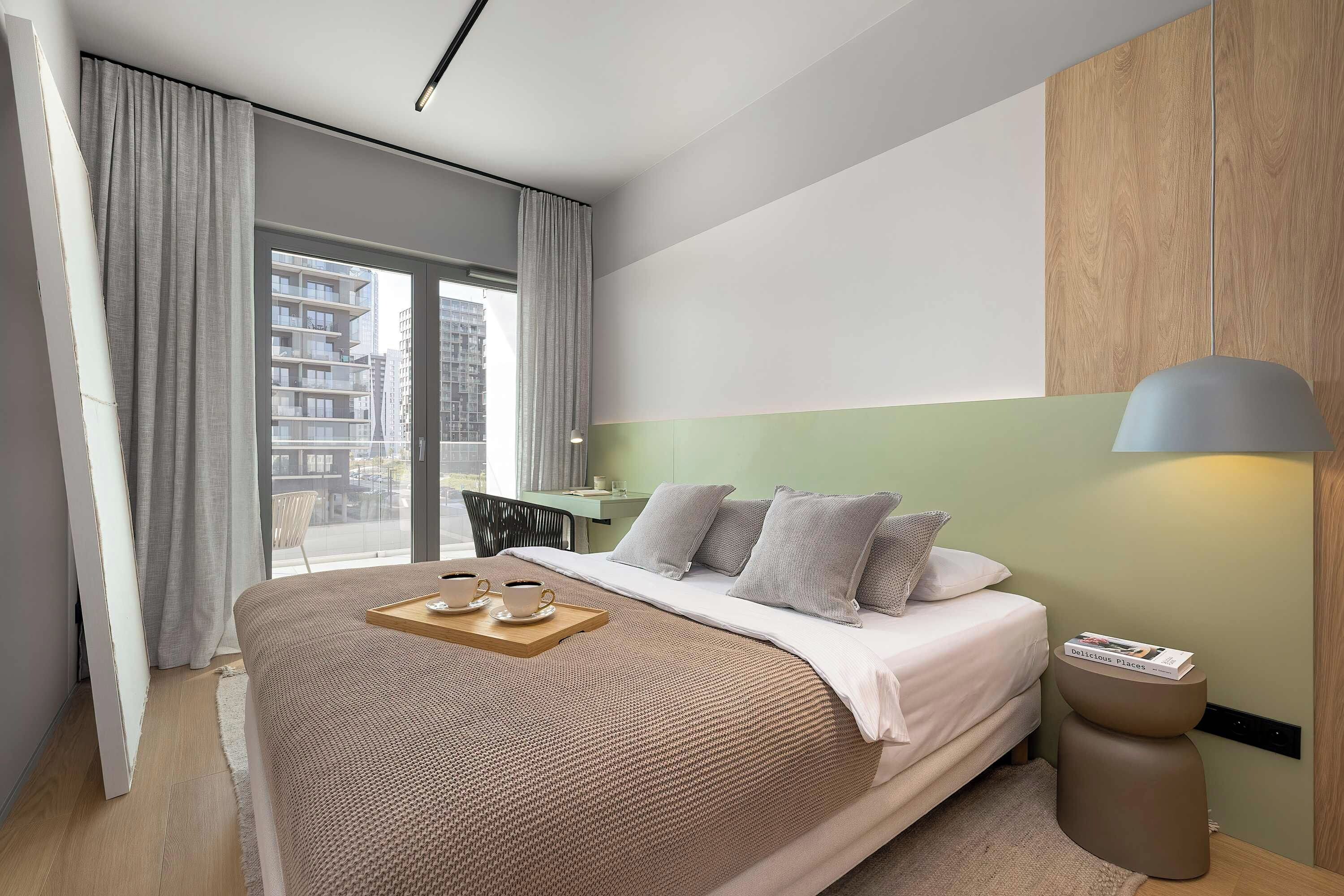 Ein modernes Hotelzimmer mit einem großen Bett, einem Nachttisch, einer Lampe und Blick auf die Stadt.
