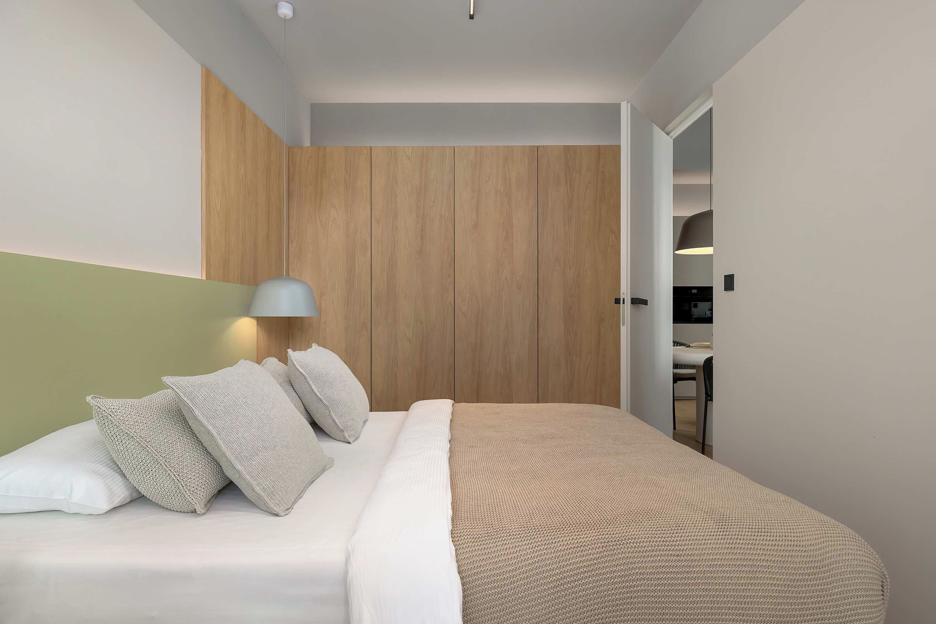 A modern bedroom with a bed, pillows, a wooden wardrobe, and a desk with a chair.