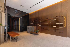A modern lobby with a bench, a reception desk, and a wall with a wooden panel design. - Elegant Apartment | Parking, Gym and Cinema in the Building (Katowice)