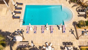 Vue aérienne d’un espace piscine comprenant des chaises longues, un transat et une table ronde.