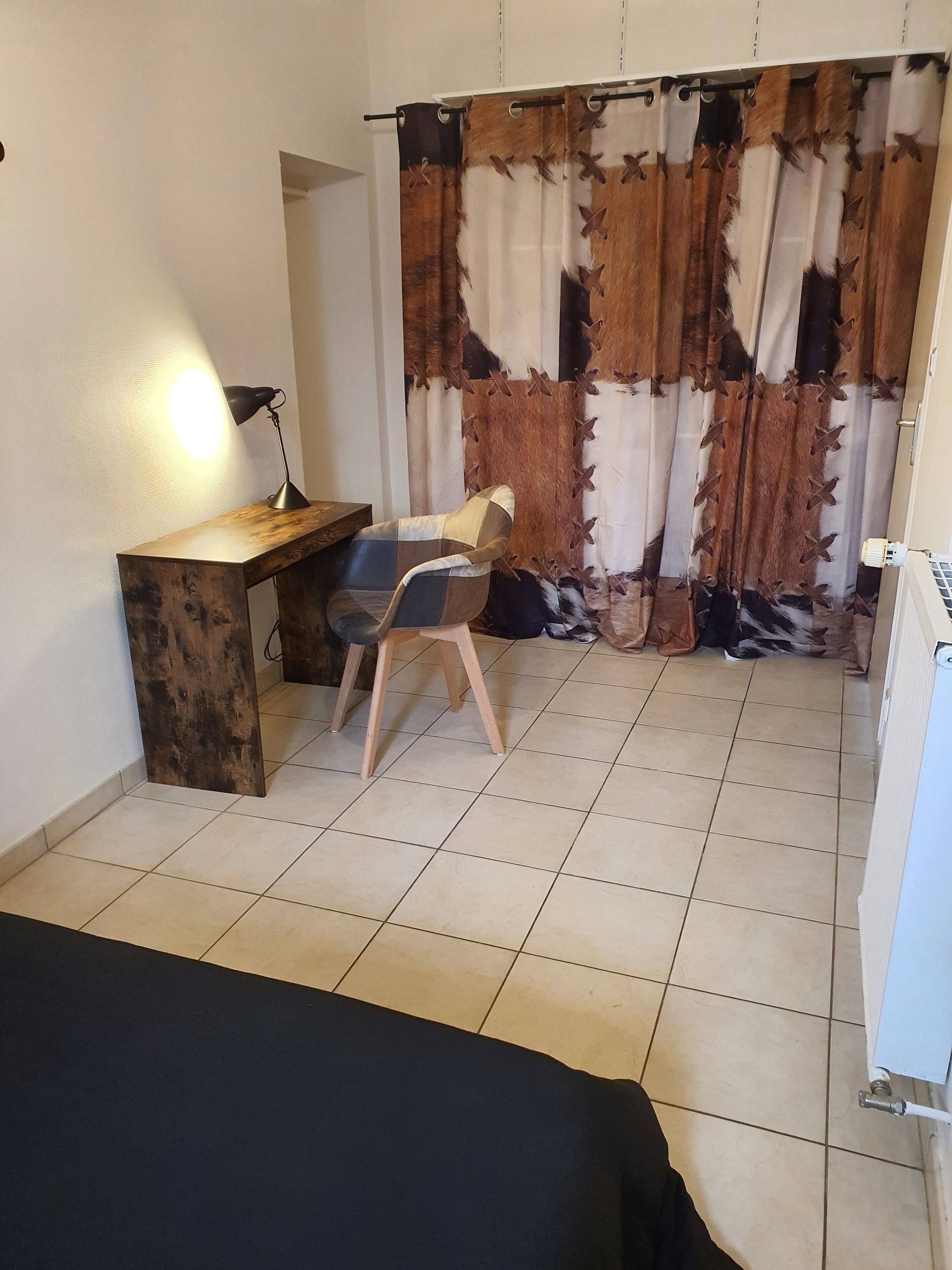 Une pièce comprenant un bureau, une chaise et un rideau orné d’un motif patchwork.