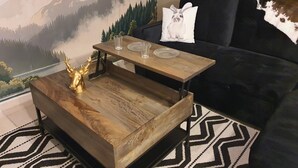 Ein Wohnzimmer mit einem Holztisch, einer schwarzen Couch und einer Wandmalerei mit Berglandschaft.