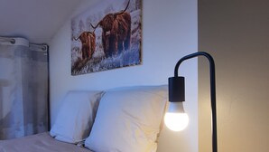 Ein Bett mit weißer Bettwäsche, ein Gemälde von Jaks an der Wand und ein Nachttisch mit Lampe.