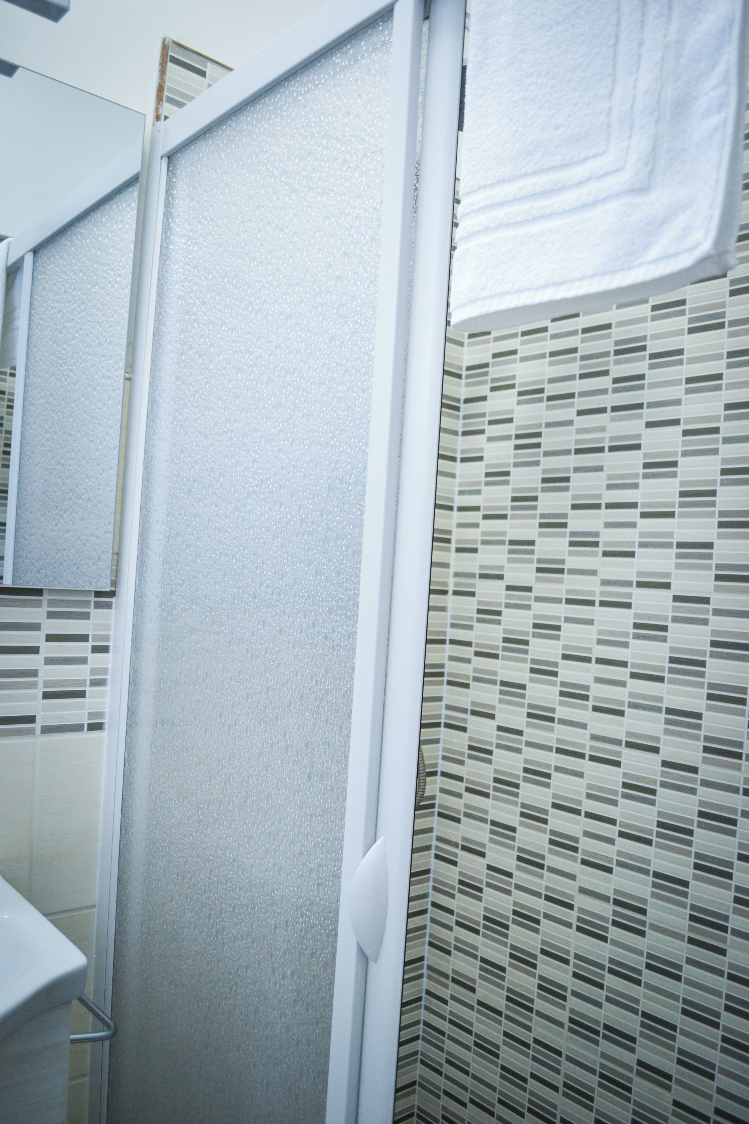 Une salle de bain avec un espace douche, un mur carrelé et une serviette blanche accrochée au mur.