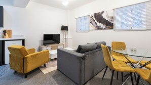 Een moderne woonkamer met een bank, gele stoelen, een glazen tafel, een televisie en kunst aan de wanden.