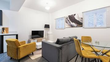 A modern living room with a sofa, yellow chairs, a glass table, a TV, and artwork on the walls.