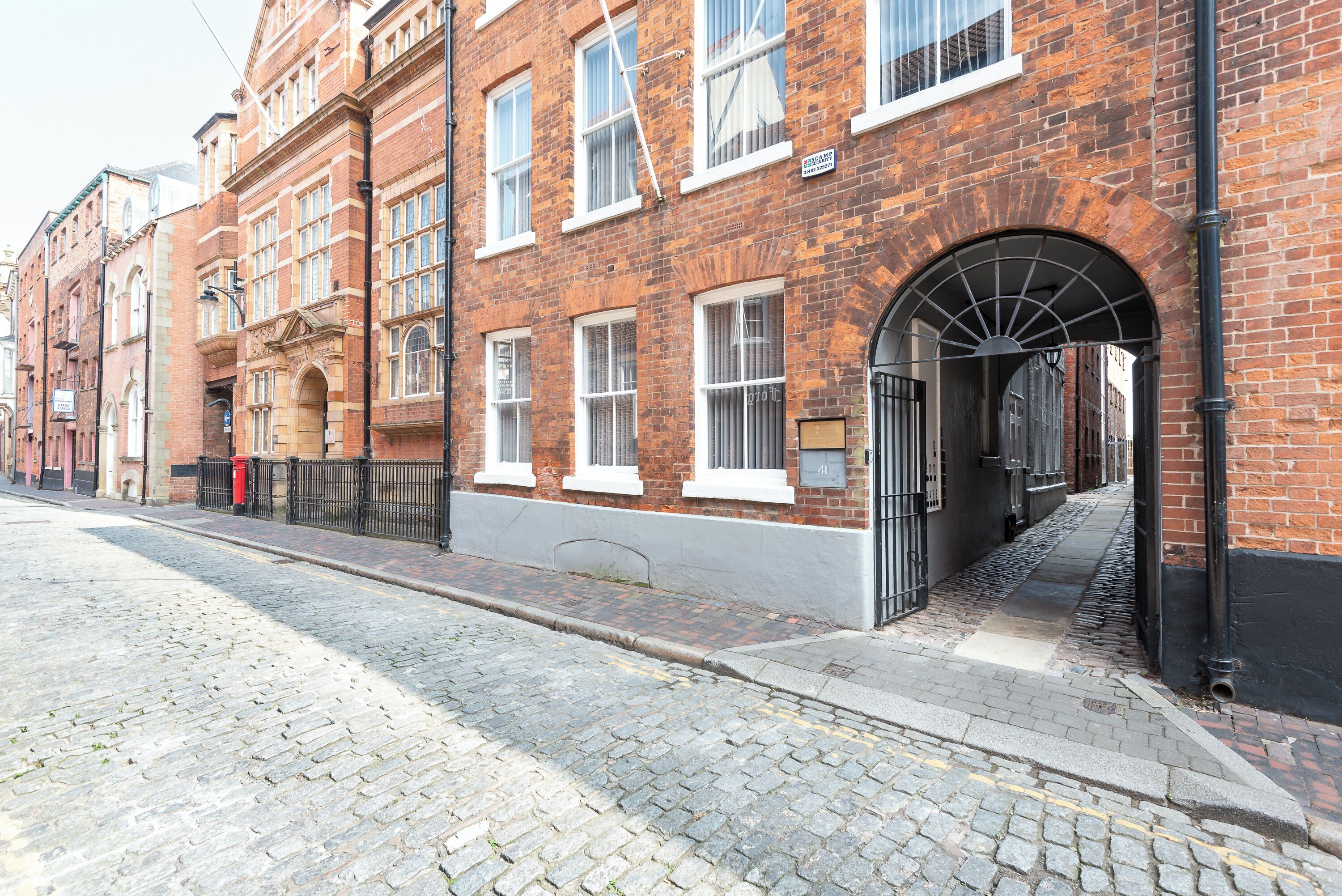 A brick building with a cobblestone street, a black metal fence, and a clear sky.