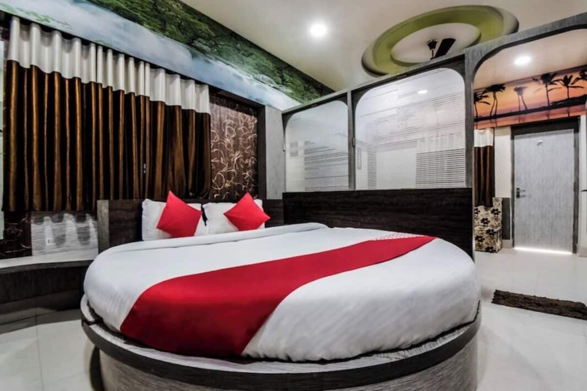 Una habitación de hotel moderna con una cama grande, un cabecero oscuro, un muro decorativo y un ventanal amplio.