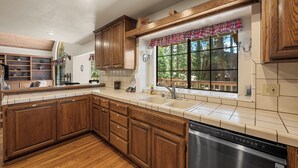 A kitchen with wooden cabinets, a dishwasher, and a window with a view of trees. - Modern Mountain Chalet w/ Hot Tub, Near the Slopes, Lake & Village (Big Bear Lake)