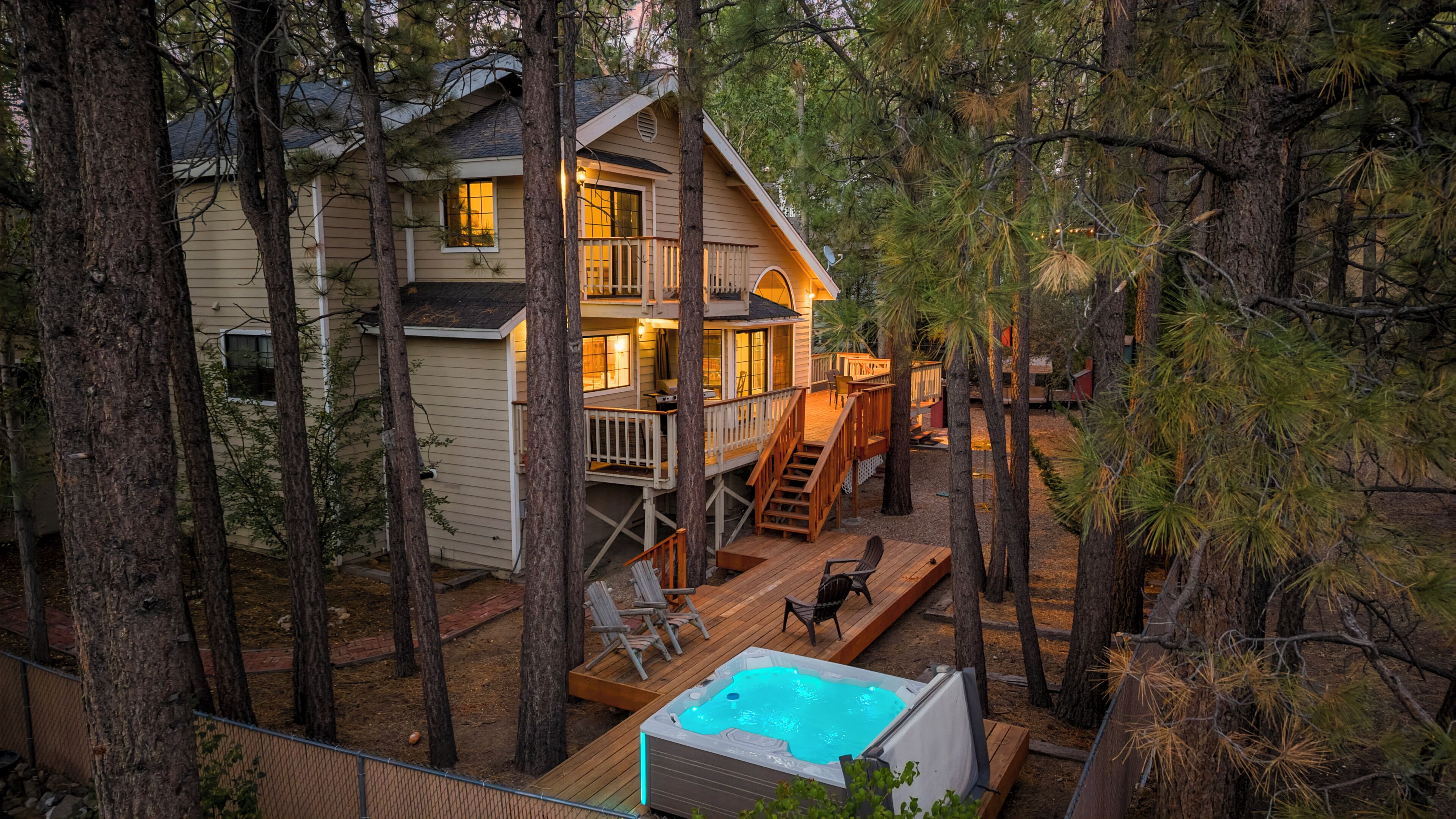 A two-story cabin with a deck, a hot tub, and a fenced-in area.