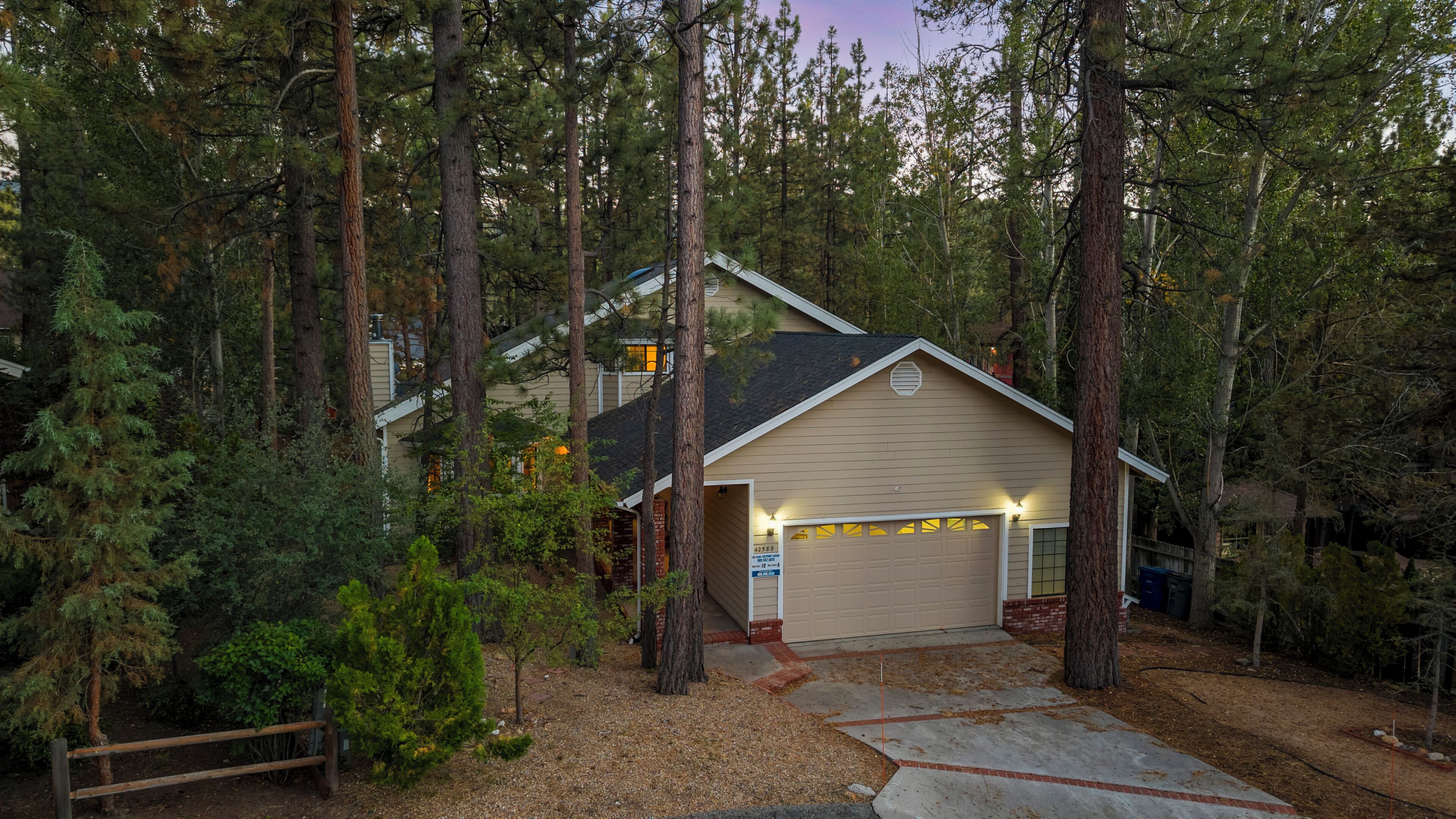 A two-story house with a garage, surrounded by tall trees and a wooden fence.