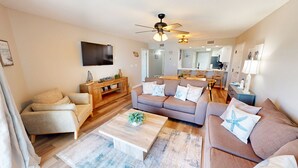 A living room with a sofa, armchair, coffee table, TV, and ceiling fan. - Seacrest 601b 2 Bedroom Condo (Fort Walton Beach)