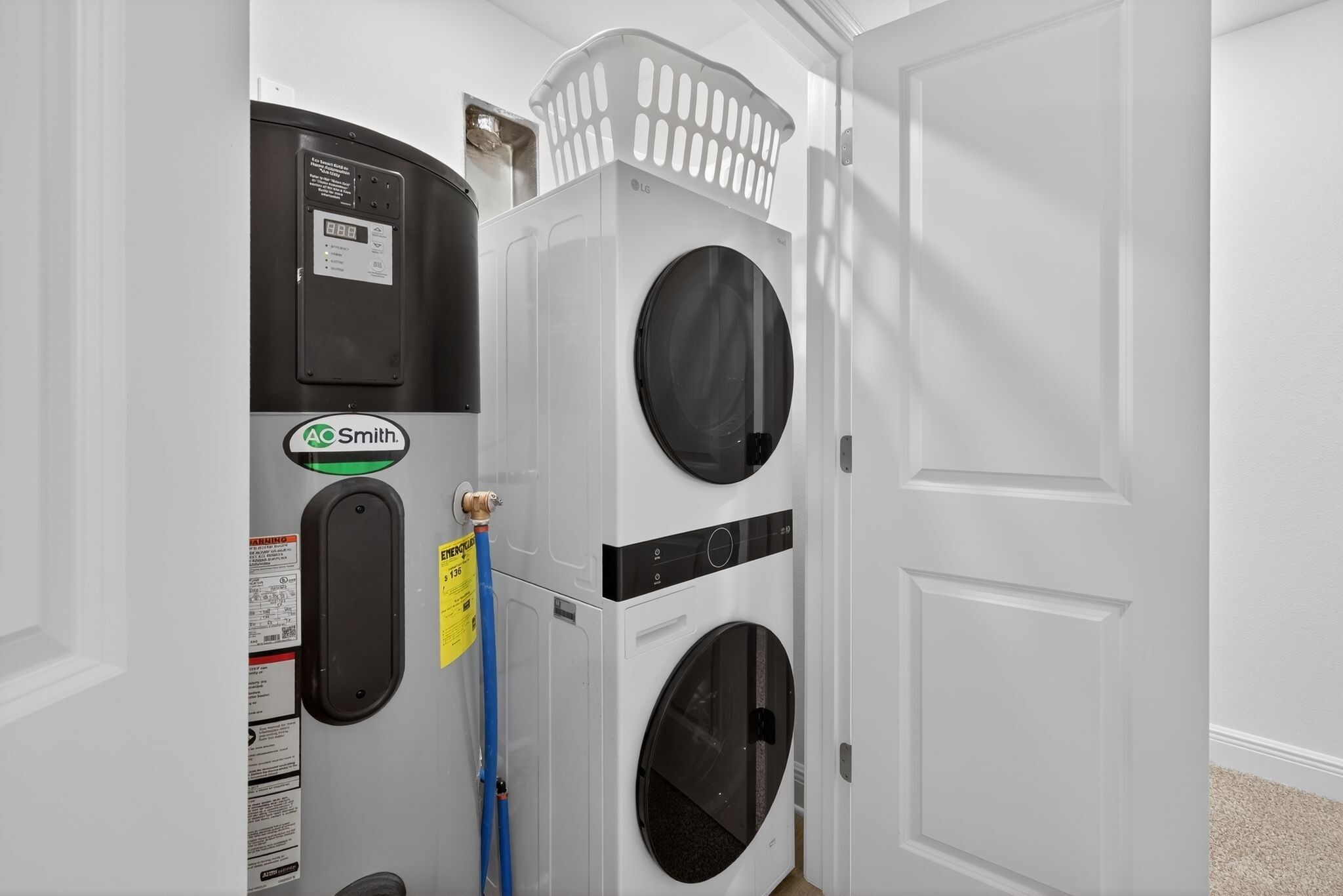 A laundry room with a front-loading washer and dryer, a basket on top of the dryer, and a blue hose.