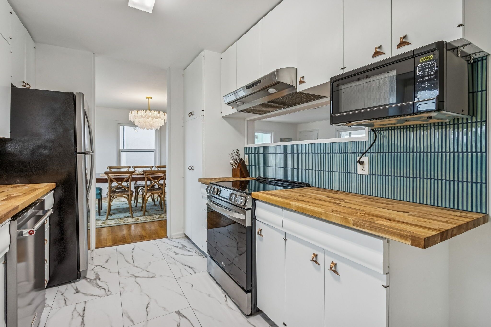 A modern kitchen with a stainless steel refrigerator, a built-in oven, a microwave, and a wooden countertop.