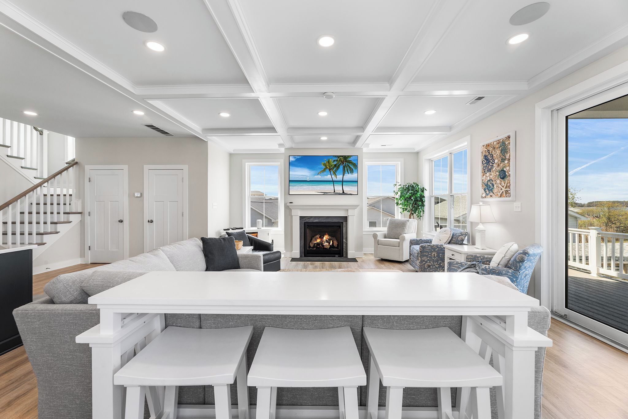 A spacious living area with a fireplace, a large dining table, and a view of the beach.