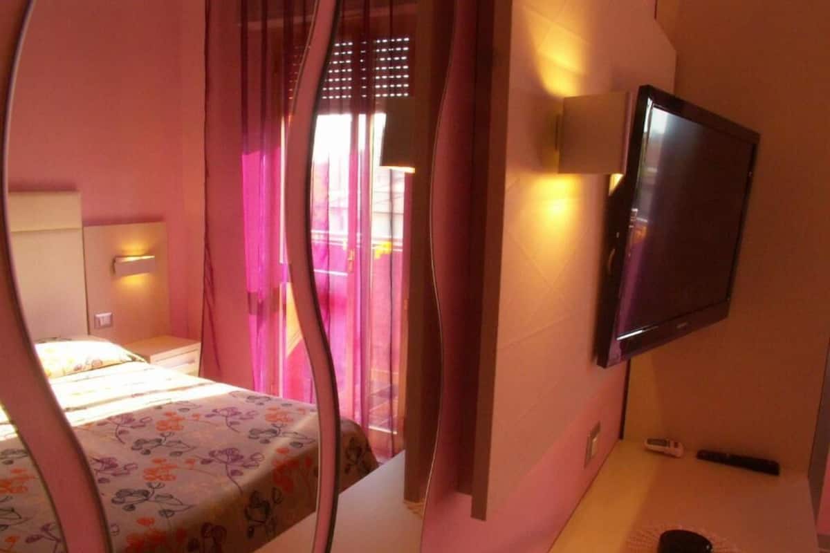 Makuuhuone, jossa on sänky, yöpöytä, televisio ja ikkuna, jossa on verhot.