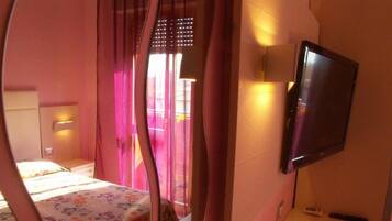 A bedroom with a bed, a bedside table, a television, and a window with curtains.